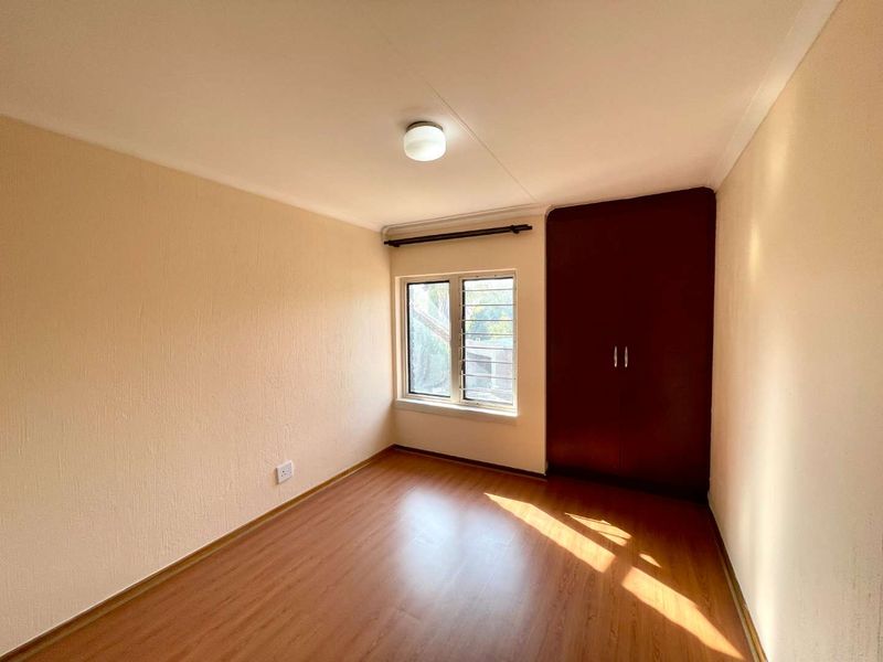 A bright, empty bedroom featuring laminate flooring, a built-in wardrobe, and a window fitted with security bars.