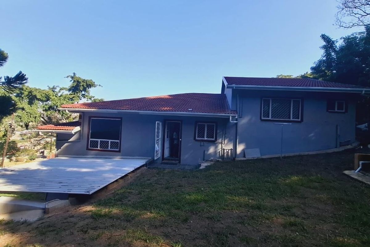 Rear view of the house featuring a tiled roof, a raised terrace area, and a sloped garden.