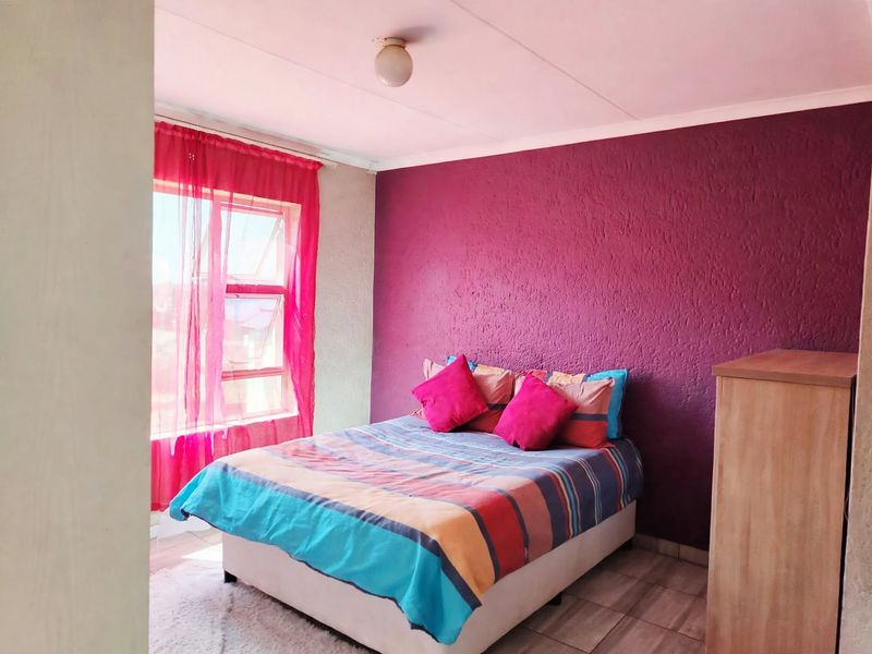 A bedroom featuring tiled flooring, a textured accent wall, and a top-hung window providing natural light.