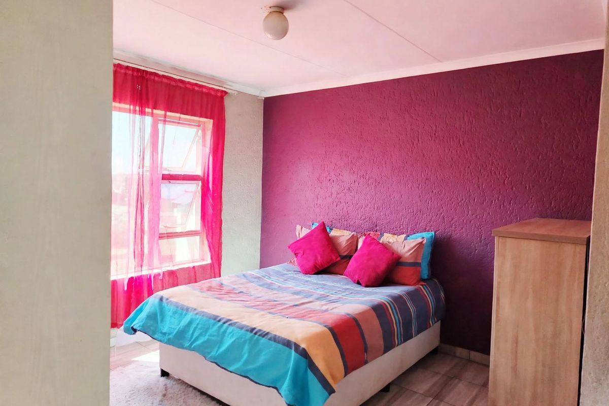A bedroom featuring tiled flooring, a textured accent wall, and a top-hung window providing natural light.