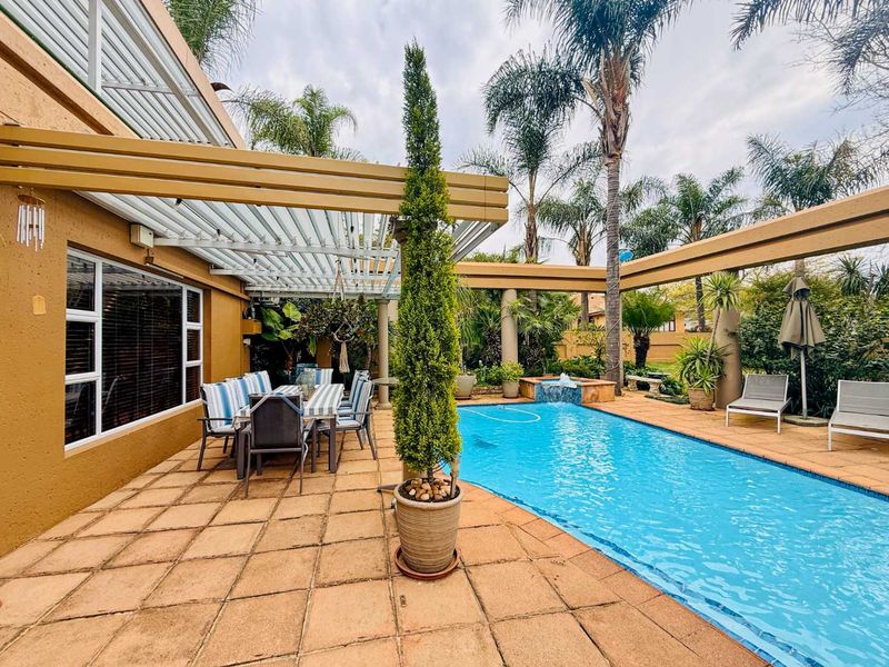 Outdoor entertainment area featuring a swimming pool, paved deck, and a covered patio with a louvre roof system.