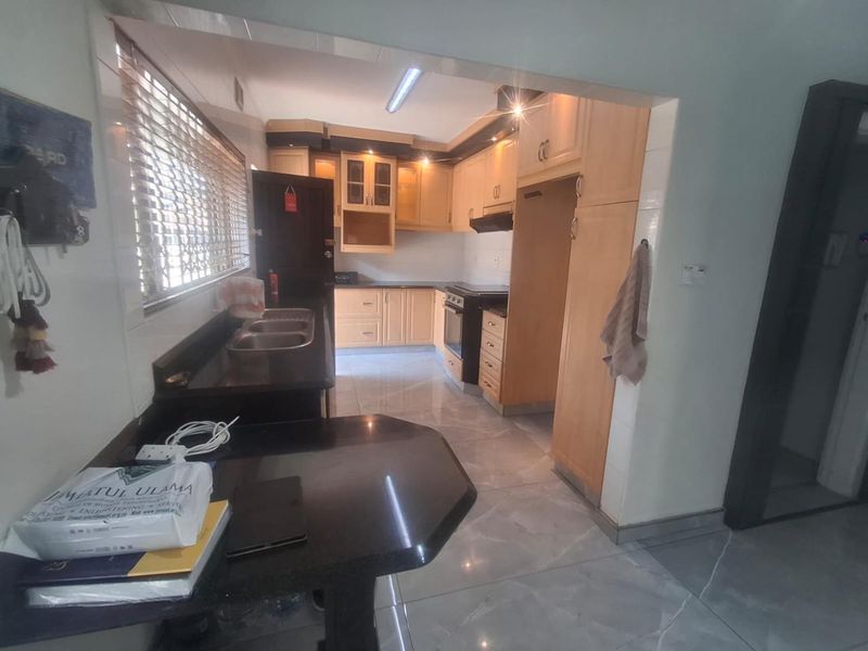 A functional kitchen featuring light wood cabinetry, dark granite countertops, built-in oven, extractor fan, and tiled flooring with security shutters on the window.