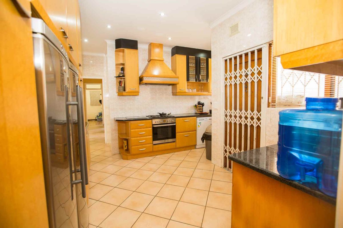 A functional kitchen featuring light wood cabinetry, granite countertops, a built-in oven, gas hob, and tiled flooring with a security gate access.