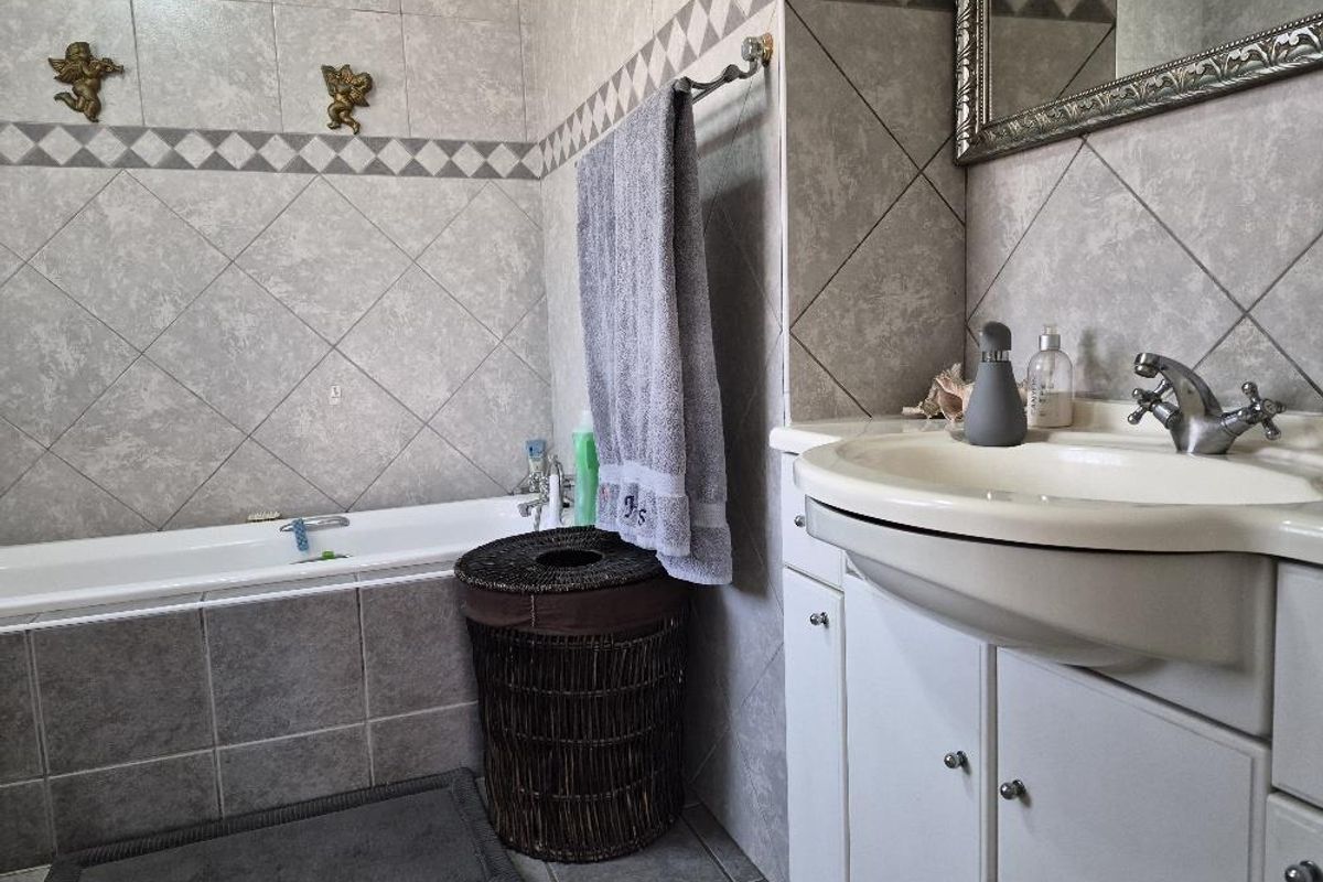 A functional bathroom featuring a built-in bathtub, a vanity cabinet with a ceramic basin, and neutral wall and floor tiling.