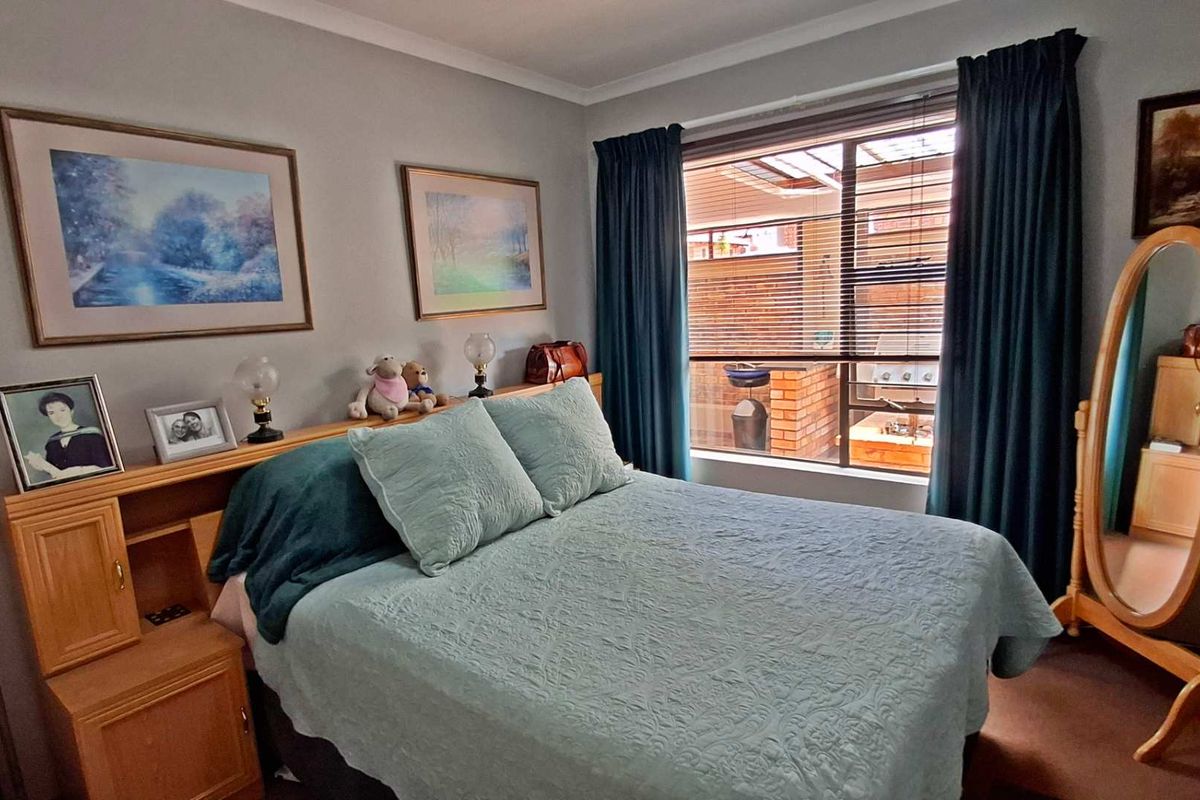 A cozy bedroom featuring a built-in wooden headboard and a window overlooking an outdoor patio area.