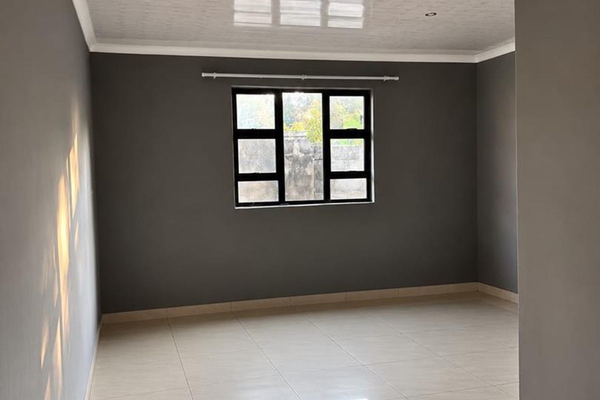 A bright, empty living room featuring neutral grey walls, large format floor tiles, and a modern glossy ceiling finish with recessed lighting.