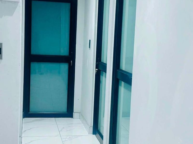 A clean, modern hallway featuring white marble-look floor tiles and sleek black aluminium framed glass doors.