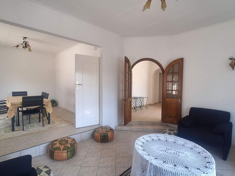 Spacious open-plan living and dining area featuring tiled flooring, a raised dining platform, and classic arched wooden double doors.
