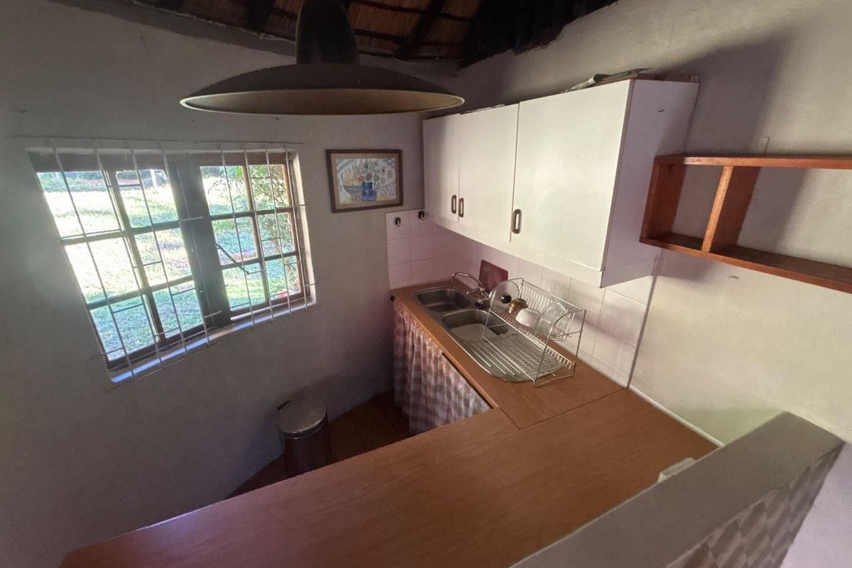 Compact kitchen area featuring a double bowl sink, laminate countertops, wall-mounted cabinetry, and a distinctive exposed thatched roof ceiling.