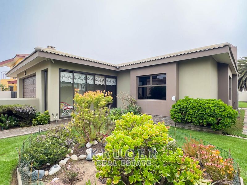 Rear view of the property featuring a well-maintained garden, paved pathways, and sliding door access to the main living area.