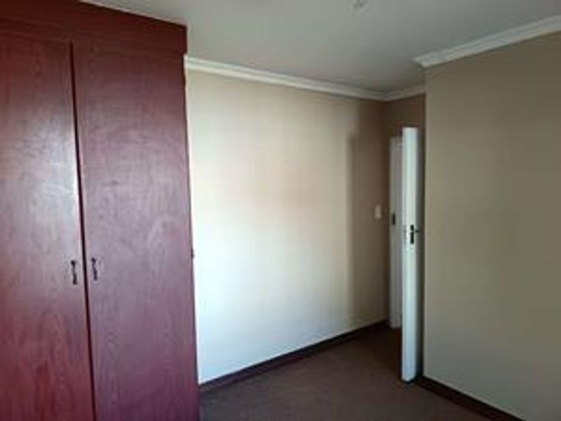 An empty bedroom featuring a built-in wooden wardrobe, neutral wall paint, and carpeted flooring.