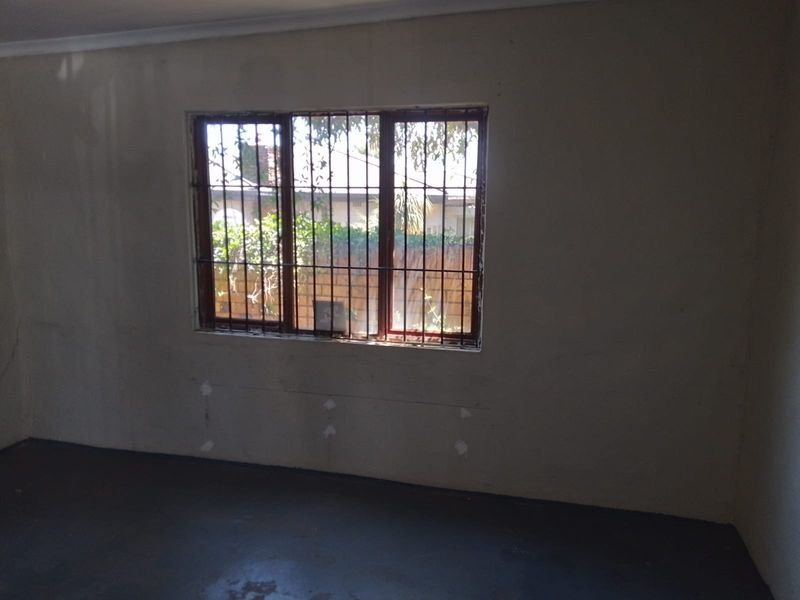 An empty, unfinished room featuring security bars on the window and visible wall plaster damage, requiring renovation and cosmetic updates.