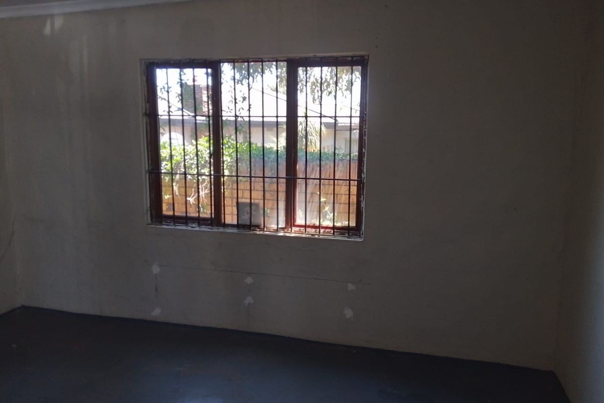 An empty, unfinished room featuring security bars on the window and visible wall plaster damage, requiring renovation and cosmetic updates.