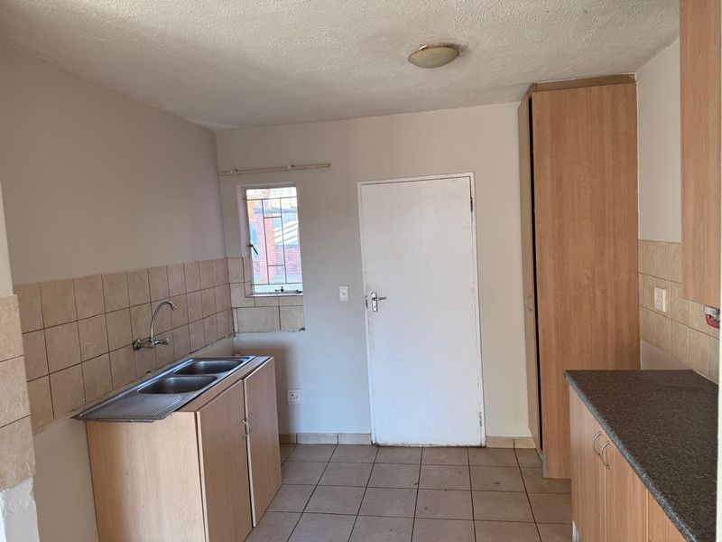 A functional kitchen space featuring laminate cabinetry, double sink, tiled splashbacks, and tiled flooring, offering a blank canvas for potential renovation.