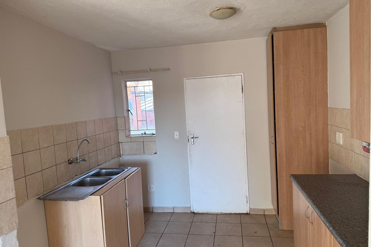 A functional kitchen space featuring laminate cabinetry, double sink, tiled splashbacks, and tiled flooring, offering a blank canvas for potential renovation.