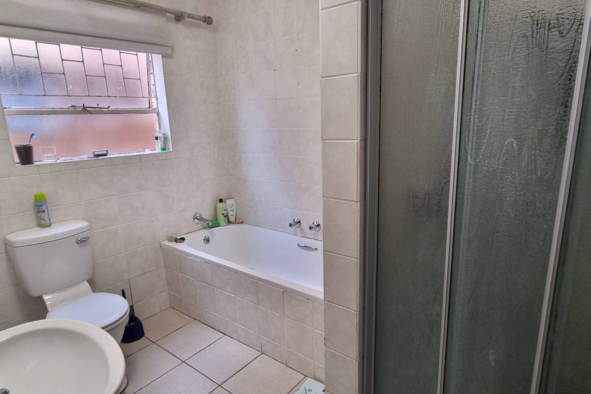 A functional bathroom featuring a built-in bathtub, separate shower enclosure, pedestal basin, and tiled finishes throughout.