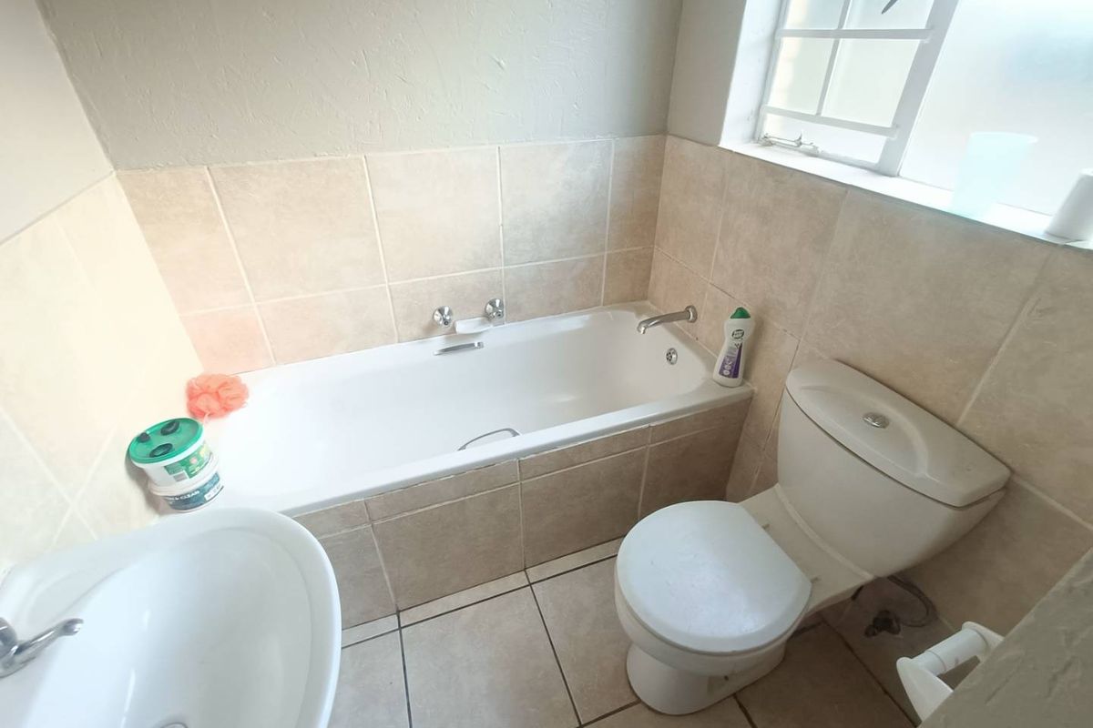 A functional bathroom featuring a built-in bathtub with tiled surround, a standard toilet, and a pedestal basin with natural light from a window.