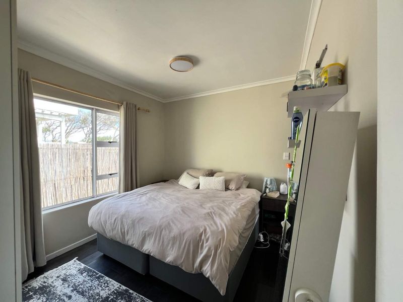 A well-lit bedroom featuring neutral wall tones, dark flooring, and a large window providing natural light.