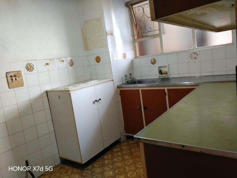 A dated kitchen featuring original cabinetry, stainless steel sink, and tiled backsplash, requiring modernization and renovation to improve functionality and aesthetic appeal.