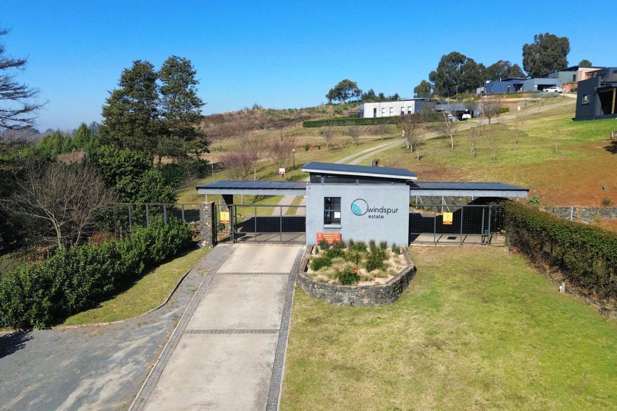 Aerial view of the Windspur Estate entrance gate, featuring a modern security guardhouse, paved driveway, and landscaped surroundings within the residential estate.