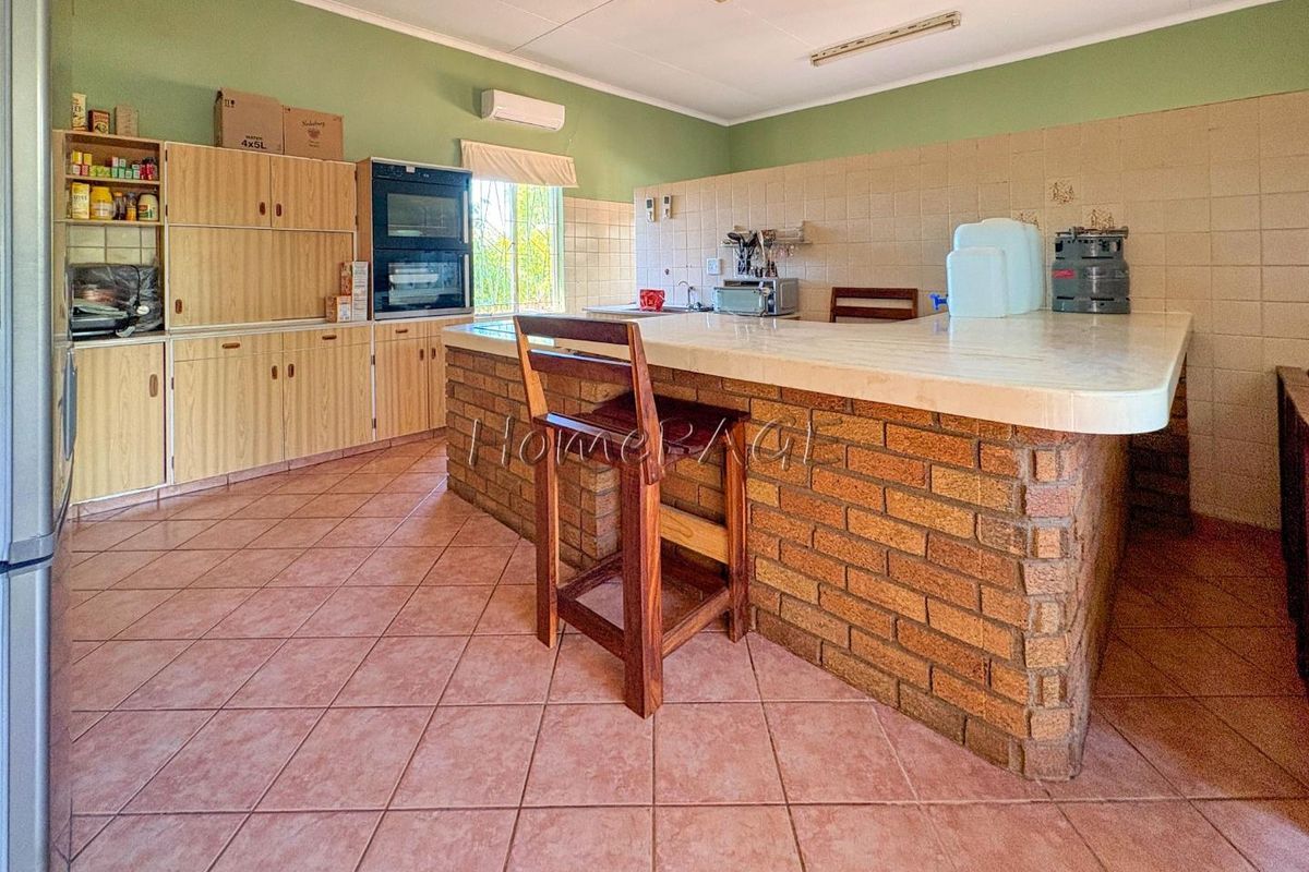 A spacious kitchen featuring a large brick-based breakfast bar, built-in wall oven, and tiled flooring with ample cabinetry for storage.