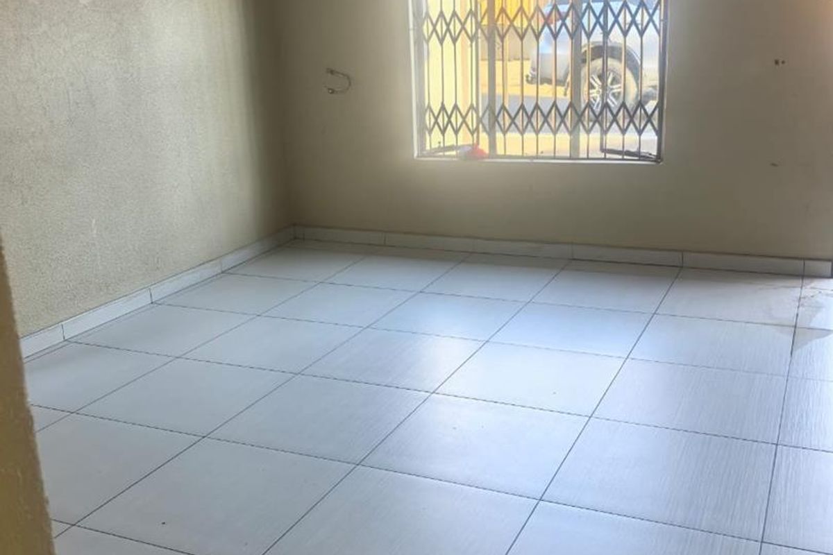 An empty living room featuring tiled flooring and a window with a security gate, requiring minor cosmetic updates to the walls.