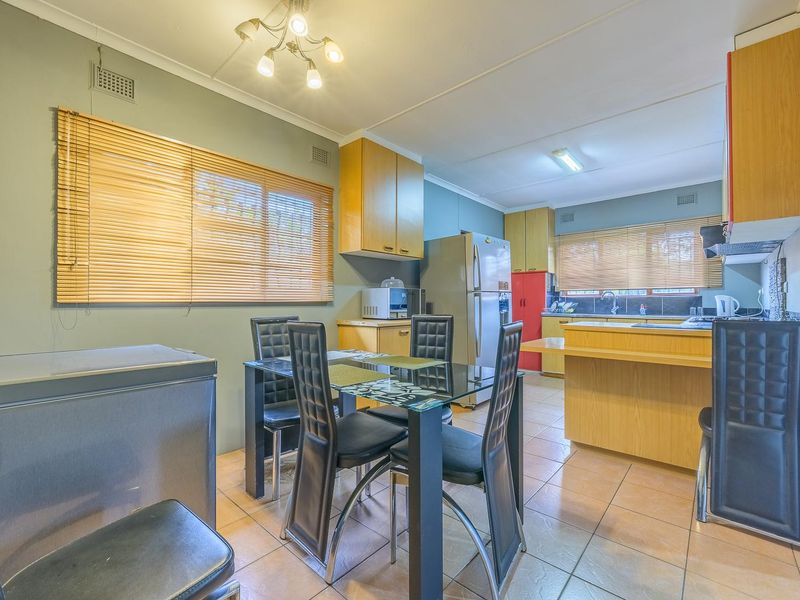 Open-plan kitchen and dining area featuring tiled flooring, built-in wooden cabinetry, and functional workspace with integrated sink and extractor fan.