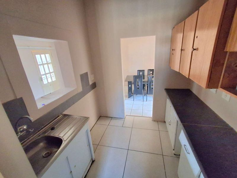 A functional scullery area featuring tiled flooring, laminate cabinetry, and a stainless steel sink, providing additional prep and wash-up space.