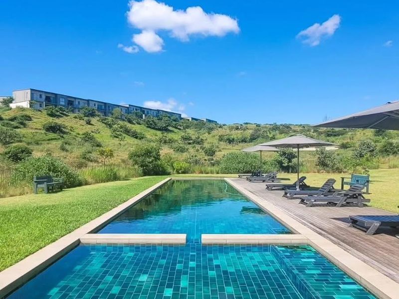 A well-maintained swimming pool featuring tiled finishes, adjacent timber decking, and a manicured lawn set against a scenic hillside backdrop.