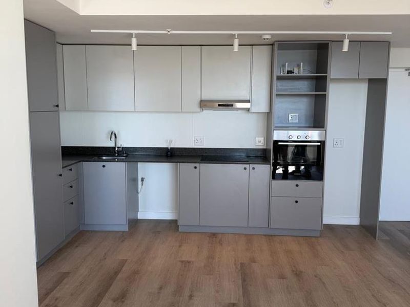 Modern kitchen featuring grey built-in cabinetry, stone countertops, integrated oven, extractor fan, and wood-look laminate flooring in an open-plan layout.