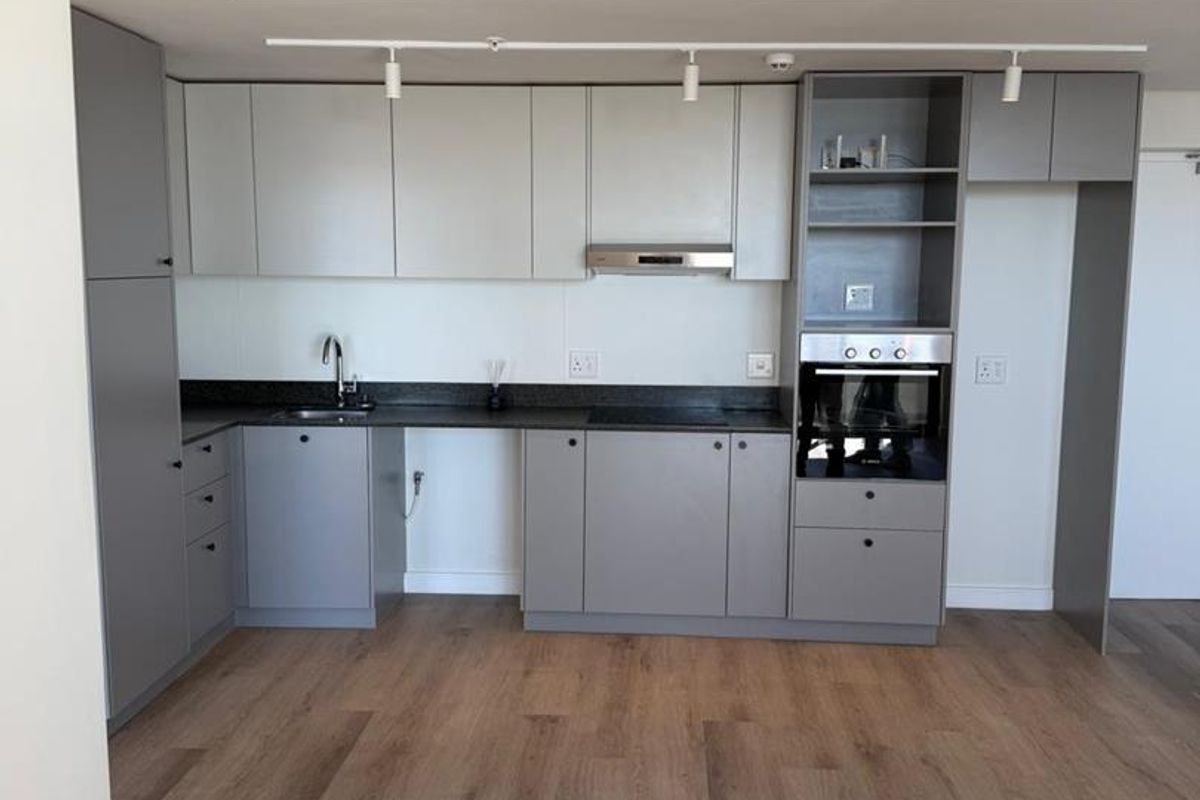 Modern kitchen featuring grey built-in cabinetry, stone countertops, integrated oven, extractor fan, and wood-look laminate flooring in an open-plan layout.