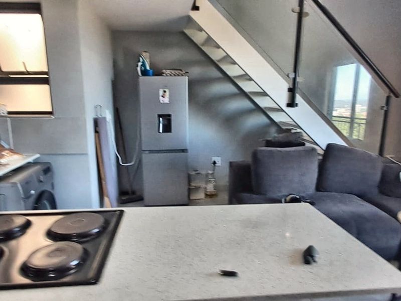 Open-plan living area featuring a modern kitchen with built-in hob and a staircase with glass balustrade leading to the upper level.
