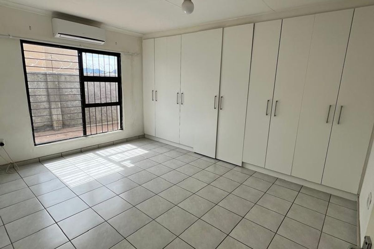 A bright bedroom featuring large built-in white wardrobes, tiled flooring, and a wall-mounted air conditioning unit.
