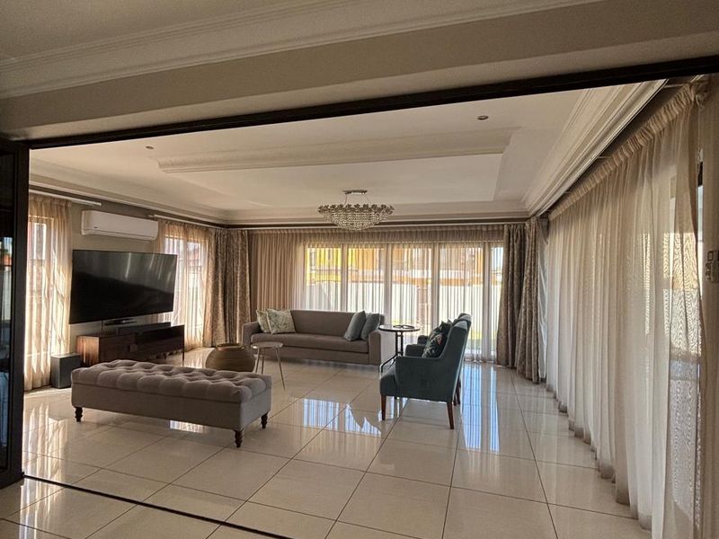 Spacious living room featuring large format porcelain floor tiles, recessed ceiling with crown molding, and expansive sliding glass doors providing ample natural light.
