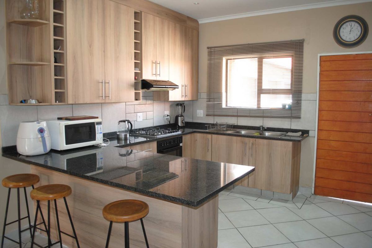 A functional kitchen featuring light wood cabinetry, dark granite countertops, a built-in gas hob, oven, extractor fan, and tiled flooring.