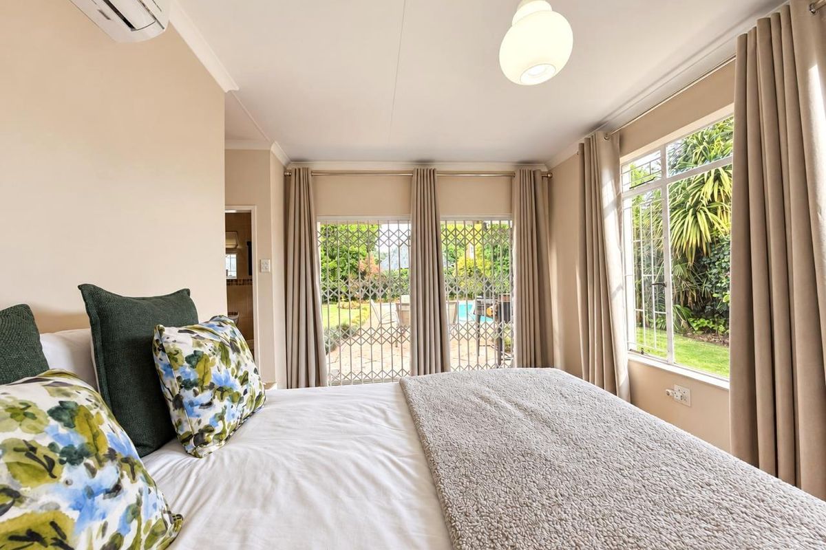 A bright bedroom featuring an air conditioning unit, pendant lighting, and direct access to the garden through a security gate and sliding glass door.