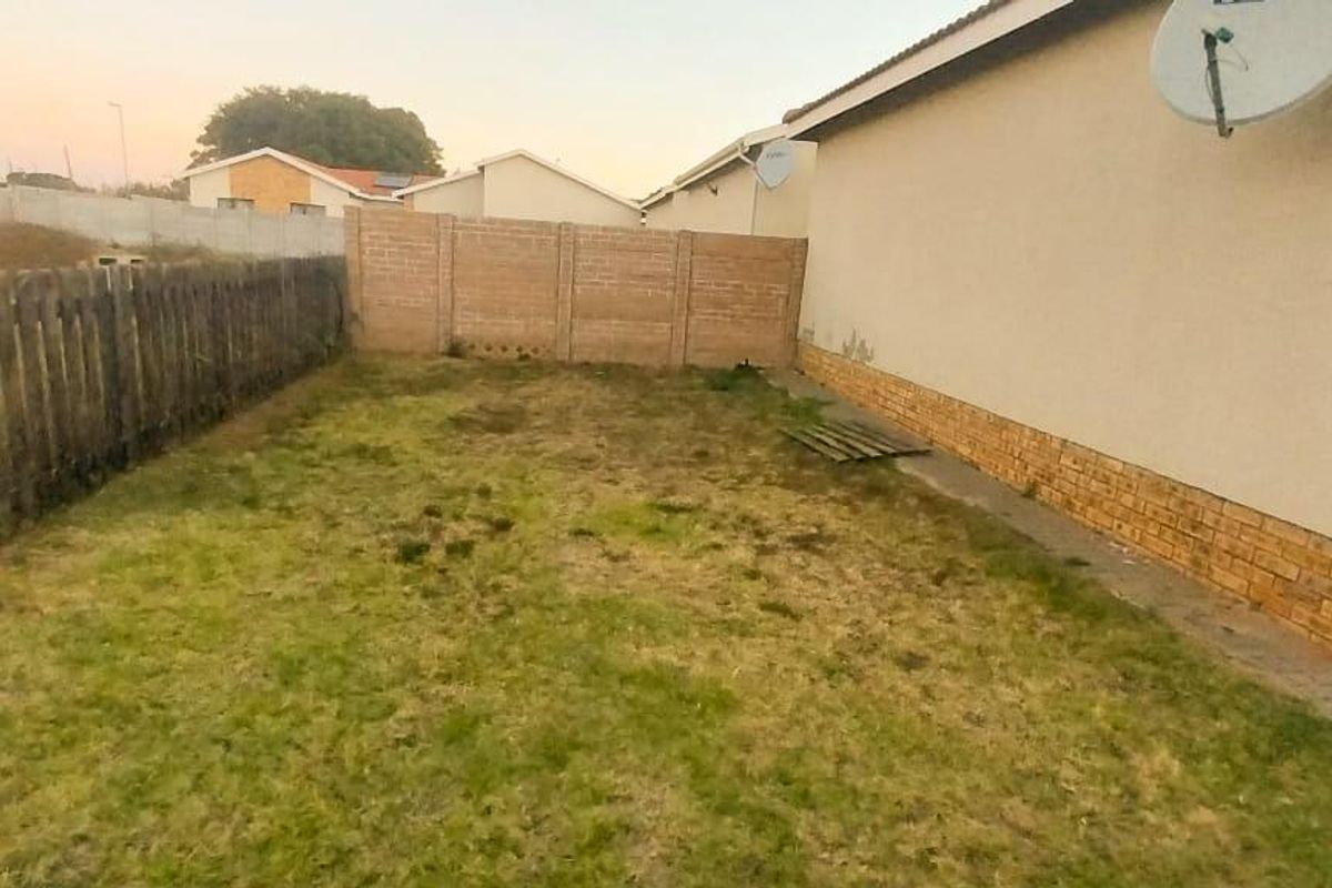 A view of the rear garden area featuring a perimeter fence, brick wall base, and satellite dish mounted on the exterior wall.