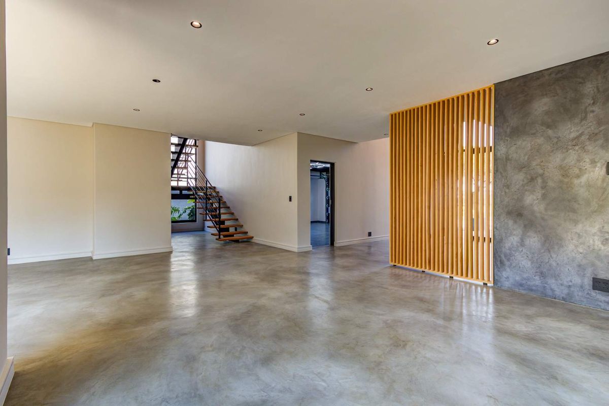Spacious open-plan living area featuring polished concrete floors, a modern timber slat room divider, and an architectural open-tread staircase.