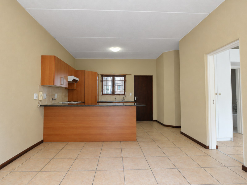 An open-plan kitchen area featuring wooden cabinetry, a breakfast counter, and ceramic tiled flooring, offering a functional layout ready for modern updates.