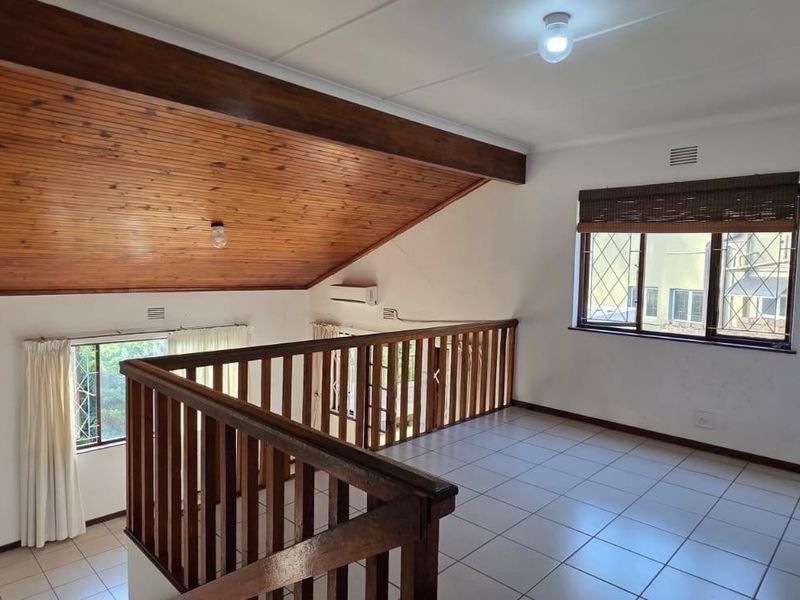 An open-plan mezzanine living area featuring a high timber raked ceiling, tiled flooring, and a timber balustrade overlooking the lower level.