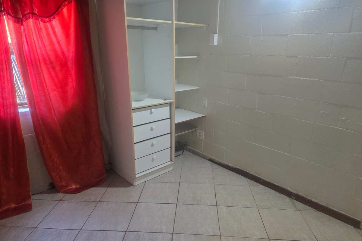 A bedroom featuring built-in cabinetry, tiled flooring, and exposed blockwork walls, offering a functional space ready for cosmetic updates.