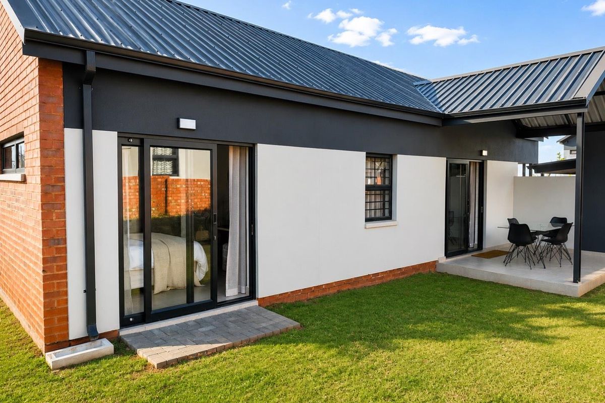 Rear view of the townhouse featuring a modern facade, metal roof, sliding glass doors, and a covered patio area overlooking the private garden.