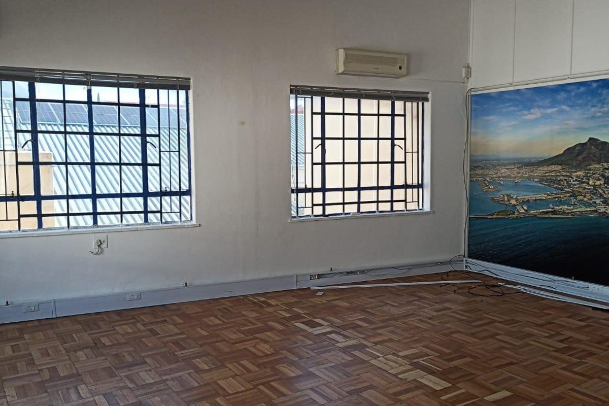 An empty living area featuring parquet flooring, security-barred windows, and a wall-mounted air conditioning unit.