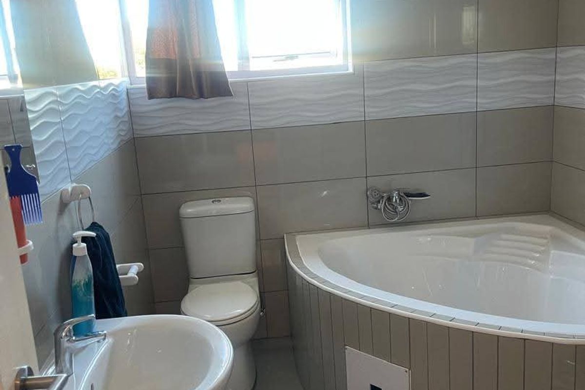 A functional bathroom featuring a corner bathtub, pedestal basin, and toilet with neutral wall and floor tiling.