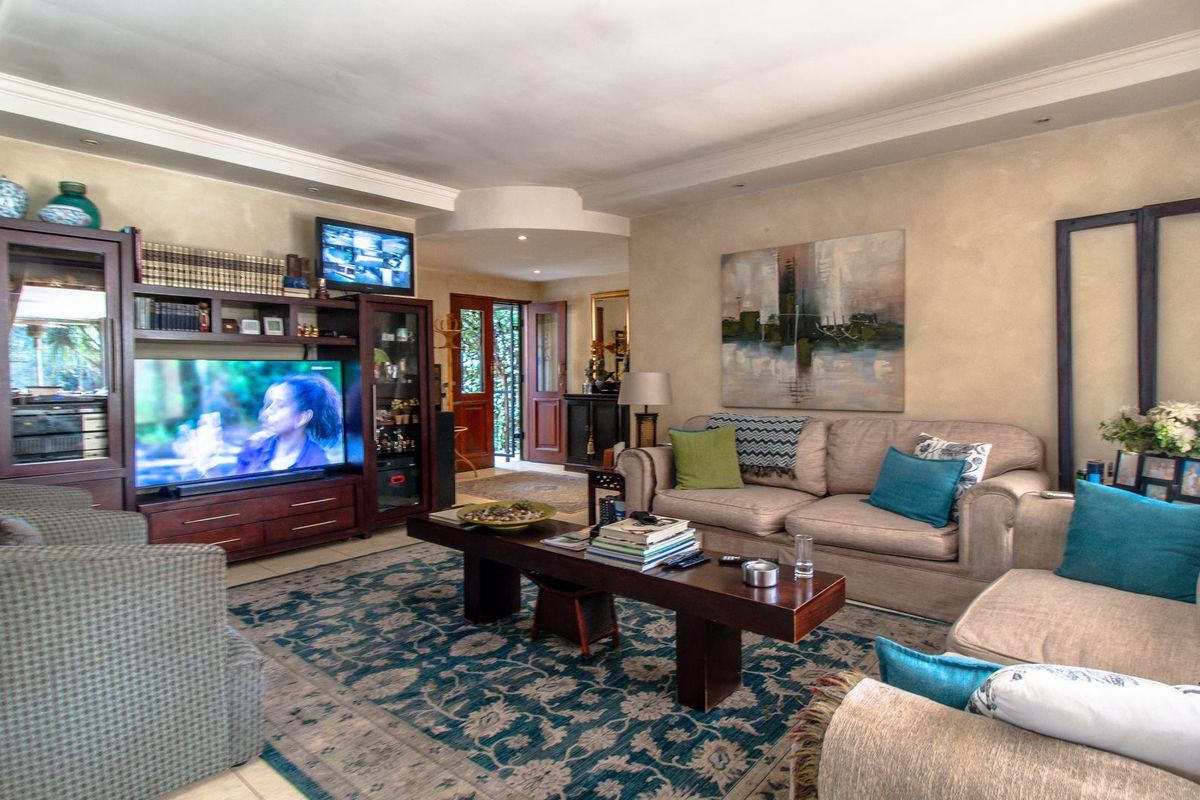 A spacious living room featuring tiled flooring, a recessed ceiling with cove lighting, and a double door entrance leading to the exterior.