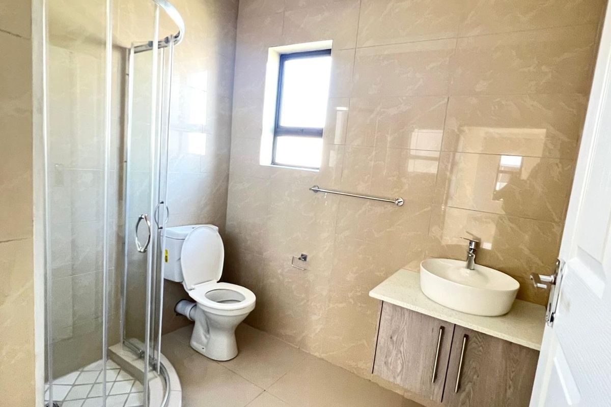 Modern bathroom featuring a glass-enclosed corner shower, a wall-mounted vanity with a vessel sink, and neutral floor-to-ceiling wall tiles.