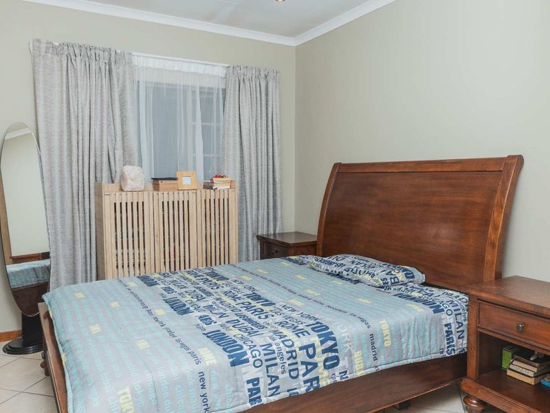 A functional bedroom featuring neutral wall tones, tiled flooring, and a built-in radiator cover beneath the window.
