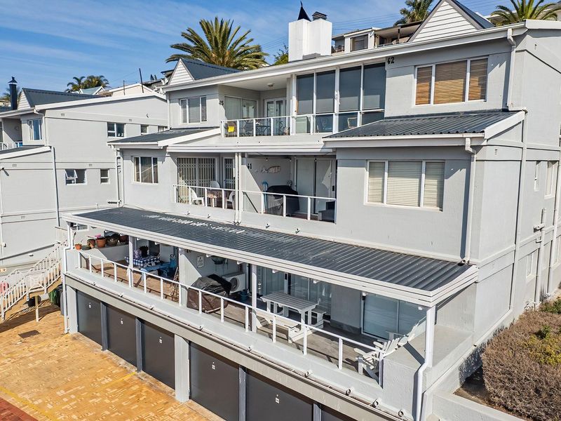 An elevated view of the rear facade of a multi-level apartment complex featuring tiered balconies, metal roofing, and ground-level garage access.