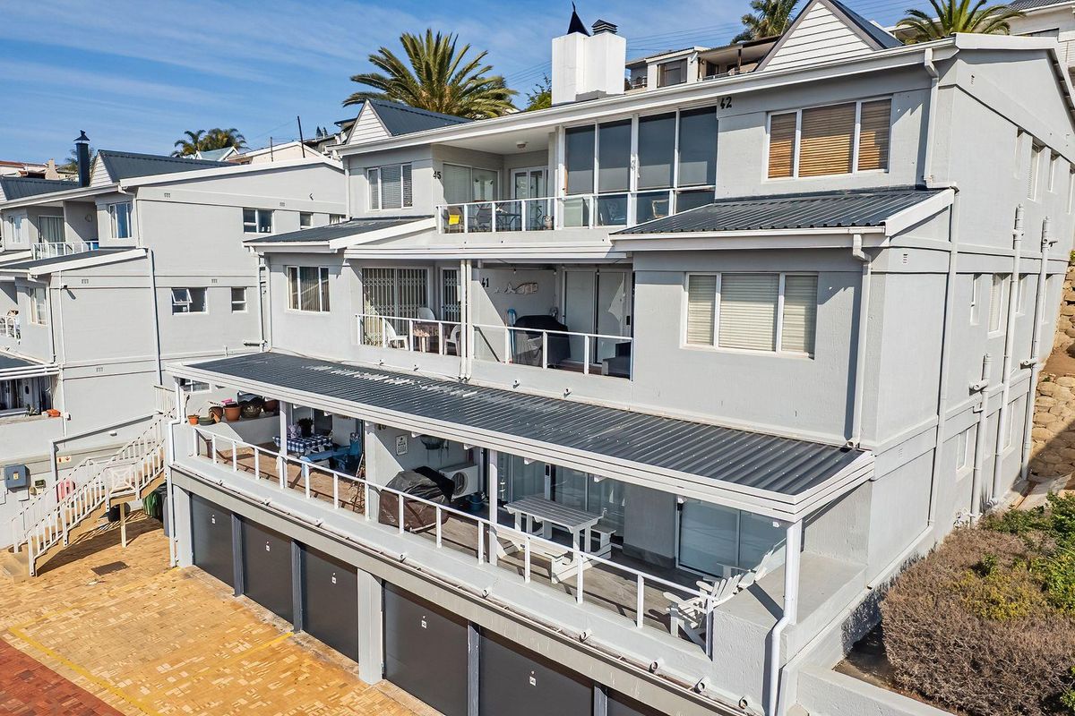 An elevated view of the rear facade of a multi-level apartment complex featuring tiered balconies, metal roofing, and ground-level garage access.