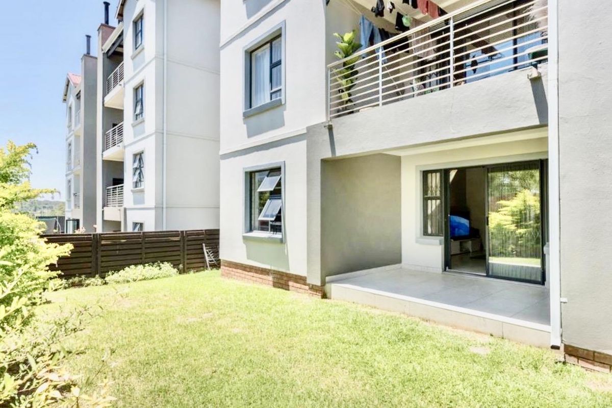 Rear view of the apartment building featuring a ground-floor tiled patio, sliding door access, and a private garden area.